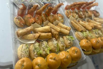 Buffet avec assortiments de sandwichs, samoussas, mini-burgers, canapés et coupes de fruits sur une table blanche.