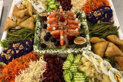 Buffet avec assortiments de sandwichs, samoussas, mini-burgers, canapés et coupes de fruits sur une table blanche.