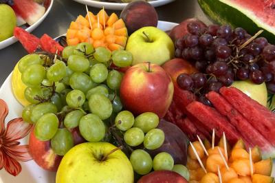 Buffet avec assortiments de sandwichs, samoussas, mini-burgers, canapés et coupes de fruits sur une table blanche.