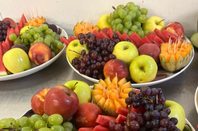 Buffet avec assortiments de sandwichs, samoussas, mini-burgers, canapés et coupes de fruits sur une table blanche.
