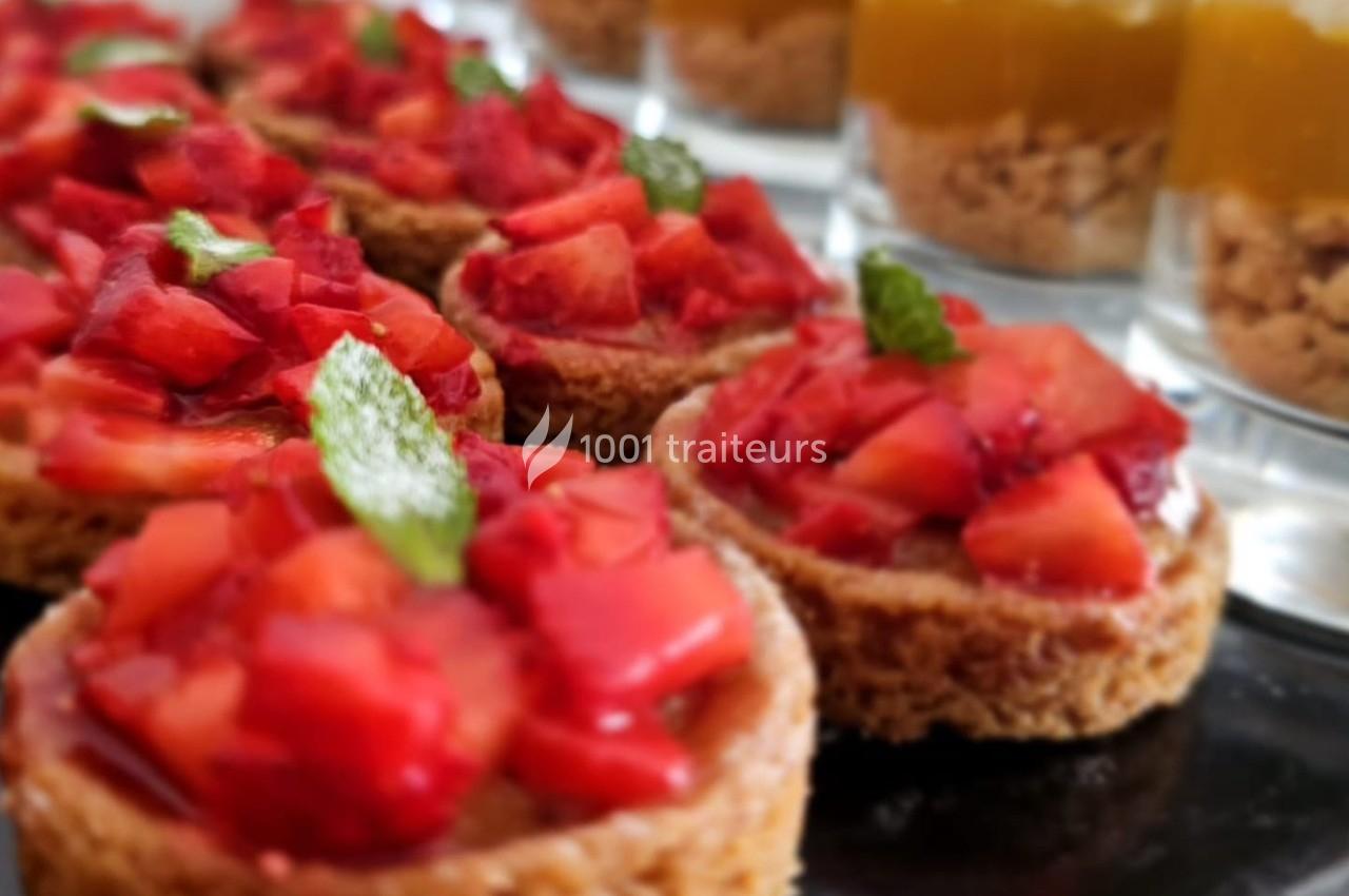Tartelettes garnies de morceaux de fraises fraîches, décorées de feuilles de menthe, avec des verrines en arrière-plan.