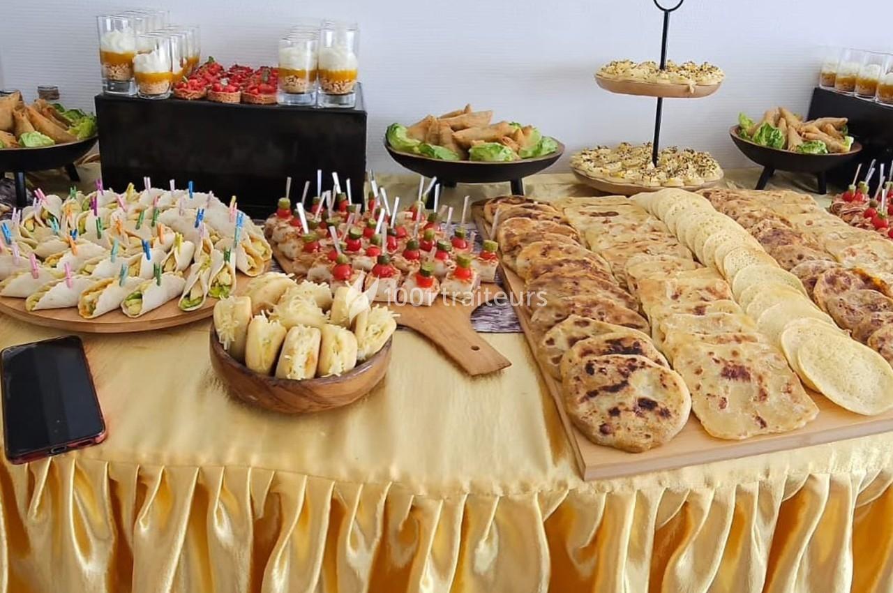 Buffet avec assortiment de mini-sandwichs, brochettes apéritives, crêpes, verrines et pâtisseries sur une nappe dorée.