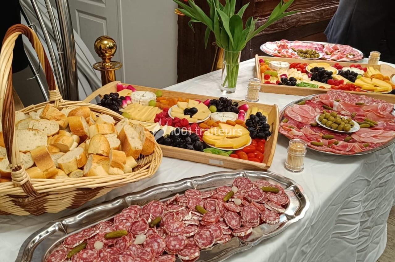 Table dressée avec des plateaux de charcuterie, fromages, fruits, pain et un bouquet de tulipes en décoration.