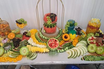 Buffet avec assortiments de sandwichs, samoussas, mini-burgers, canapés et coupes de fruits sur une table blanche.