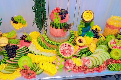 Buffet avec assortiments de sandwichs, samoussas, mini-burgers, canapés et coupes de fruits sur une table blanche.