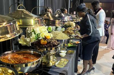 Buffet avec assortiments de sandwichs, samoussas, mini-burgers, canapés et coupes de fruits sur une table blanche.