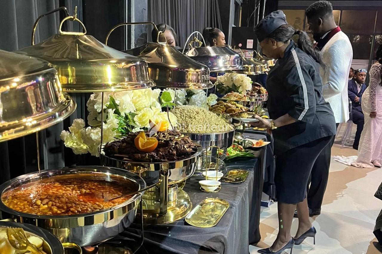 Buffet avec plats variés, incluant viande, riz et légumes, présenté dans des récipients dorés avec décorations florales.