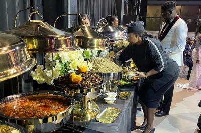 Buffet avec assortiments de sandwichs, samoussas, mini-burgers, canapés et coupes de fruits sur une table blanche.