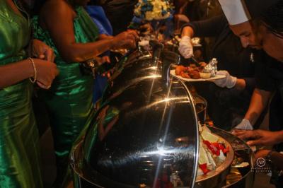 Buffet avec assortiments de sandwichs, samoussas, mini-burgers, canapés et coupes de fruits sur une table blanche.