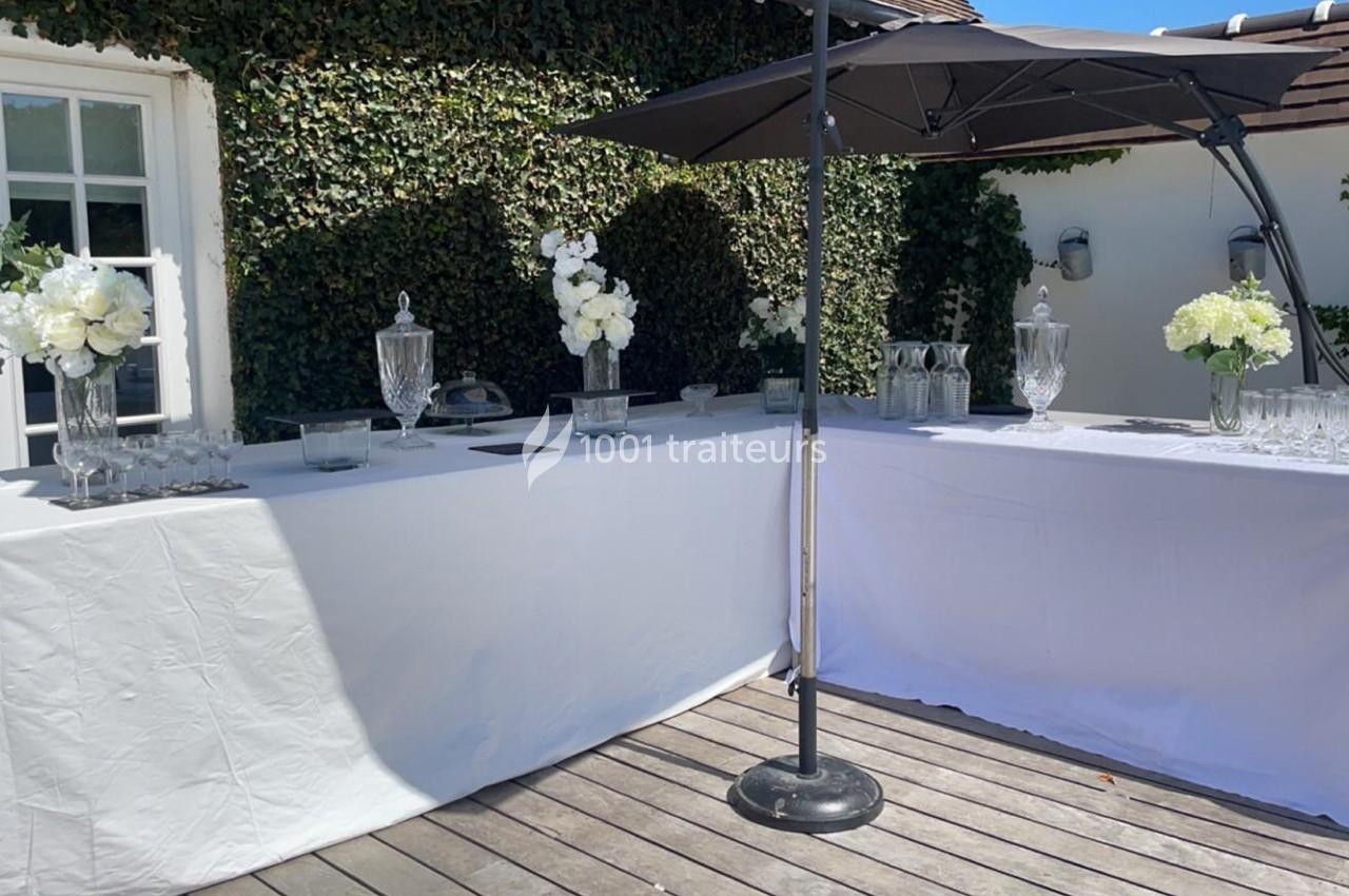 Tables drapées de blanc avec des décorations florales, des verres et des carafes sur une terrasse ensoleillée.