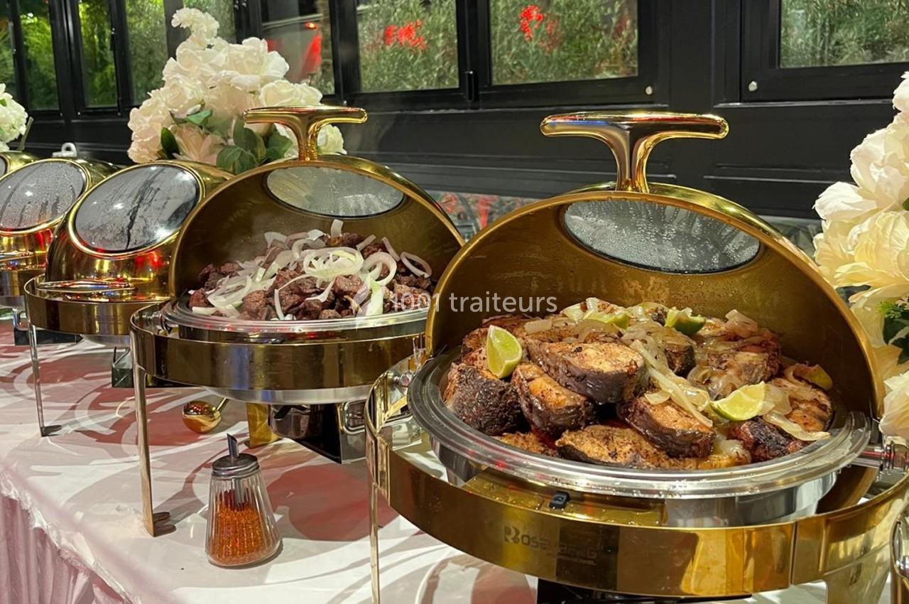 Buffet avec plats chauds présentés dans des chafing dishes dorés, incluant viandes grillées et garnitures.