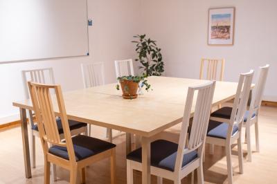 Quatre personnes discutent autour d'une table dans une salle de réunion lumineuse avec un ordinateur au centre.