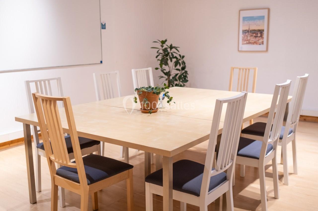 Salle de réunion lumineuse avec une grande table en bois entourée de chaises, un tableau blanc et une plante décorative.