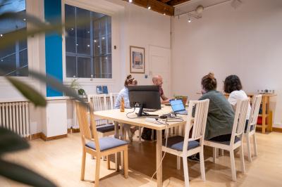 Quatre personnes discutent autour d'une table dans une salle de réunion lumineuse avec un ordinateur au centre.