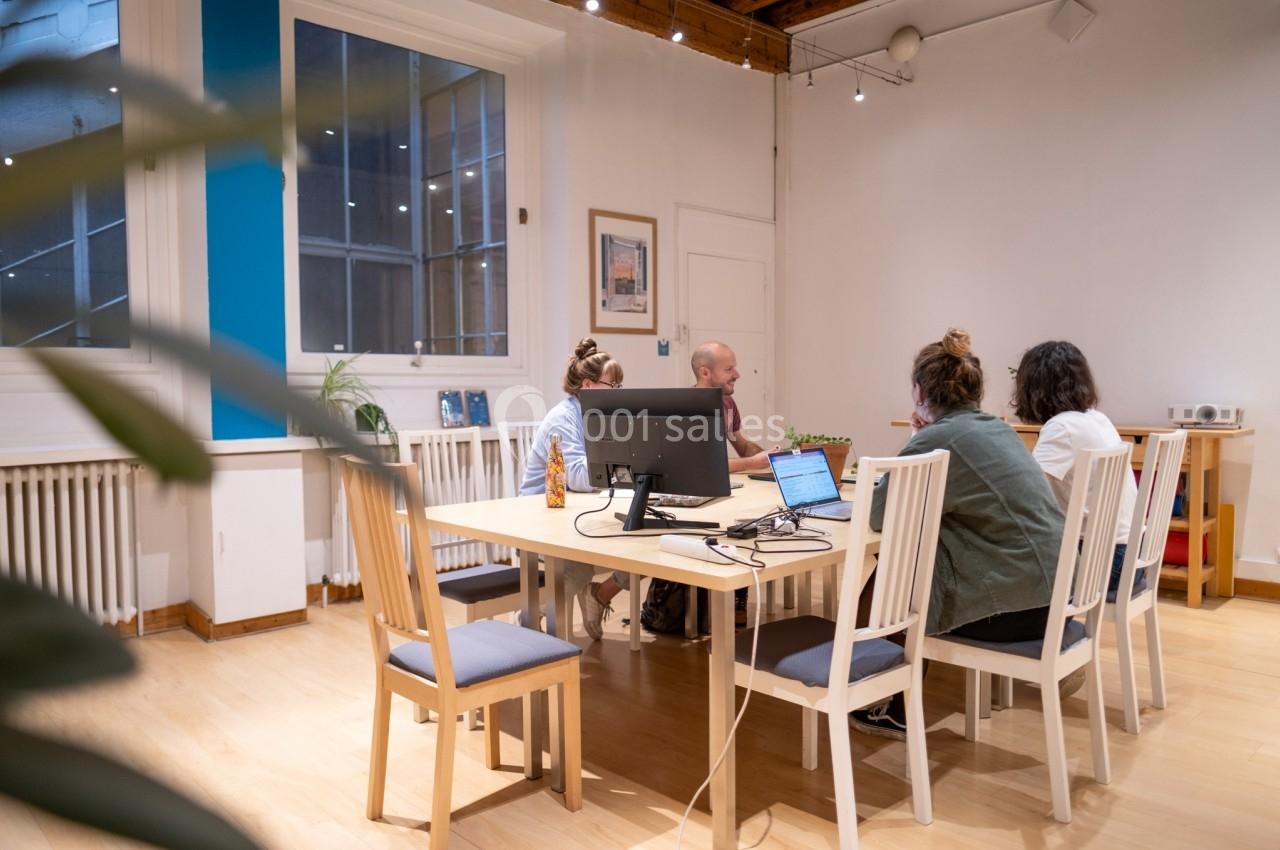 Quatre personnes discutent autour d'une table dans une salle de réunion lumineuse avec un ordinateur au centre.