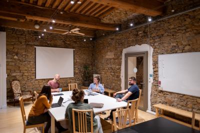 Quatre personnes discutent autour d'une table dans une salle de réunion lumineuse avec un ordinateur au centre.