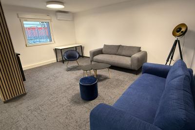 Salle de réception avec tables rondes dressées, nappes blanches, serviettes rouges et chaises grises sur parquet clair.