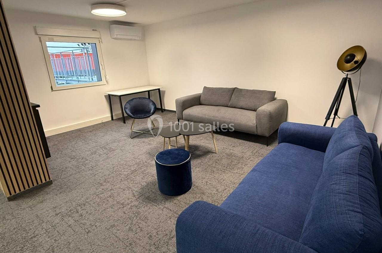 Salon moderne avec deux canapés, une table basse, un fauteuil, un tabouret et un lampadaire sur tapis gris.