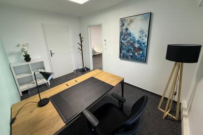 Salle de réception avec tables rondes dressées, nappes blanches, serviettes rouges et chaises grises sur parquet clair.