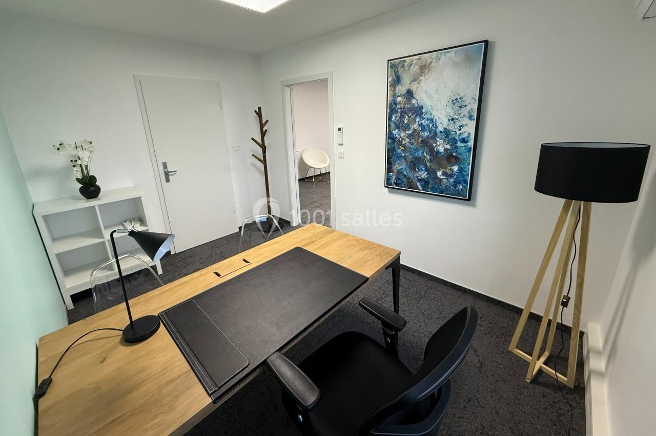 Bureau moderne avec un bureau en bois, chaise noire, lampe, étagère, tableau abstrait et porte-manteau.