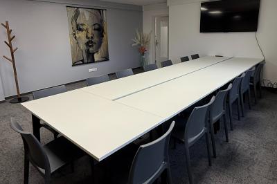 Salle de réception avec tables rondes dressées, nappes blanches, serviettes rouges et chaises grises sur parquet clair.