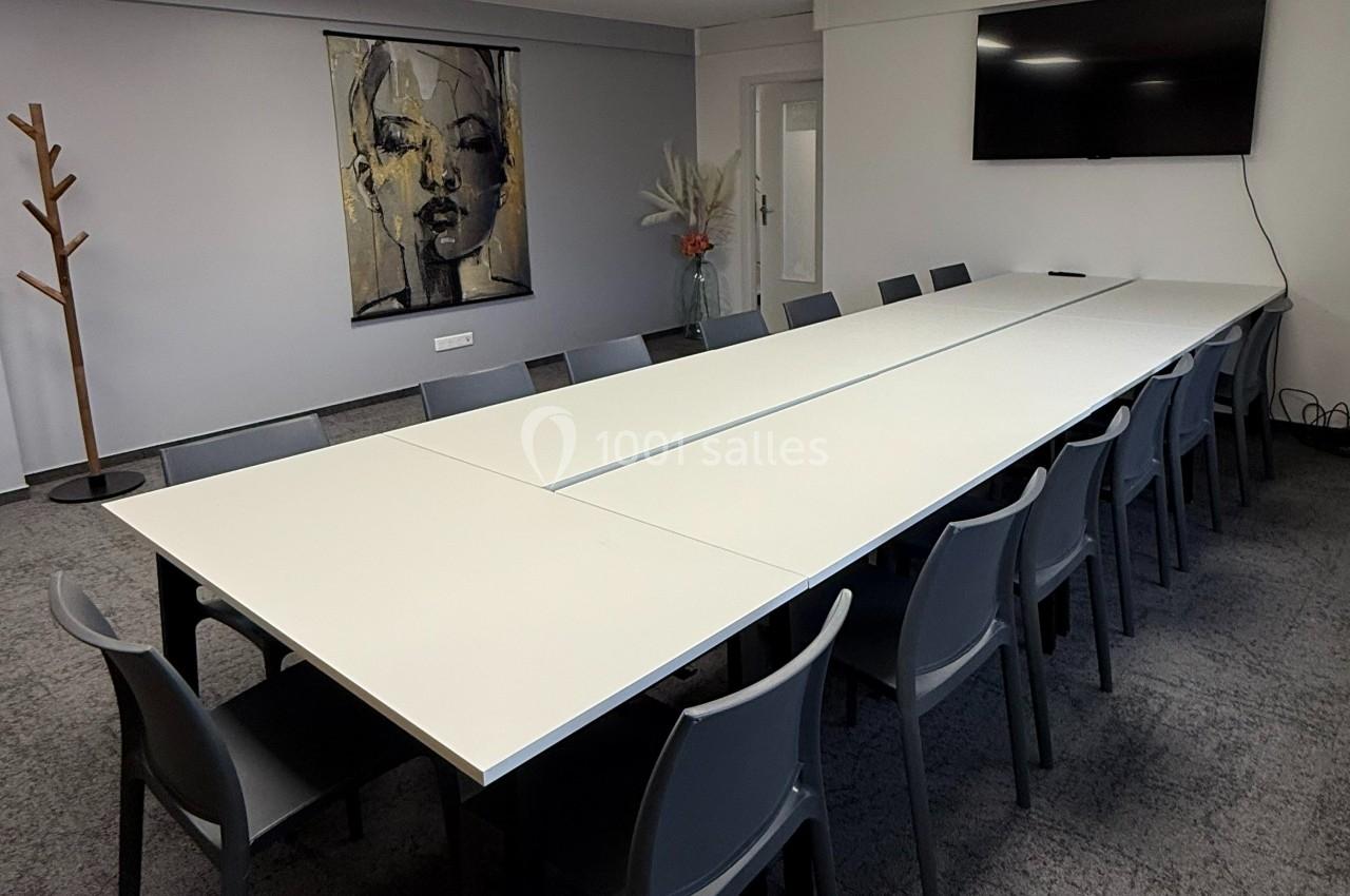 Salle de réunion moderne avec une grande table blanche, des chaises grises, un écran mural et une décoration minimaliste.