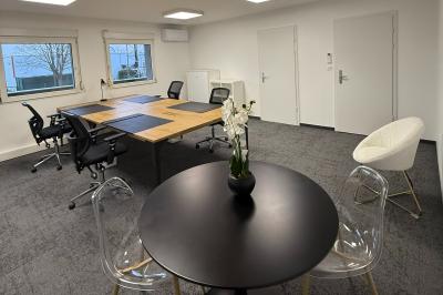 Salle de réception avec tables rondes dressées, nappes blanches, serviettes rouges et chaises grises sur parquet clair.