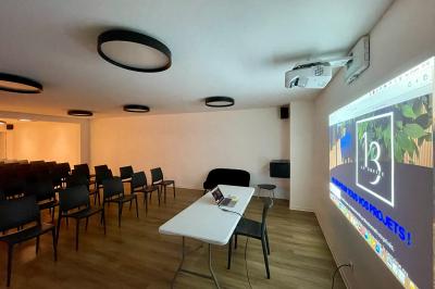 Salle de réception avec tables rondes dressées, nappes blanches, serviettes rouges et chaises grises sur parquet clair.