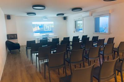 Salle de réception avec tables rondes dressées, nappes blanches, serviettes rouges et chaises grises sur parquet clair.
