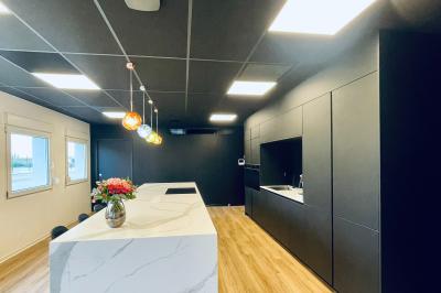 Salle de réception avec tables rondes dressées, nappes blanches, serviettes rouges et chaises grises sur parquet clair.