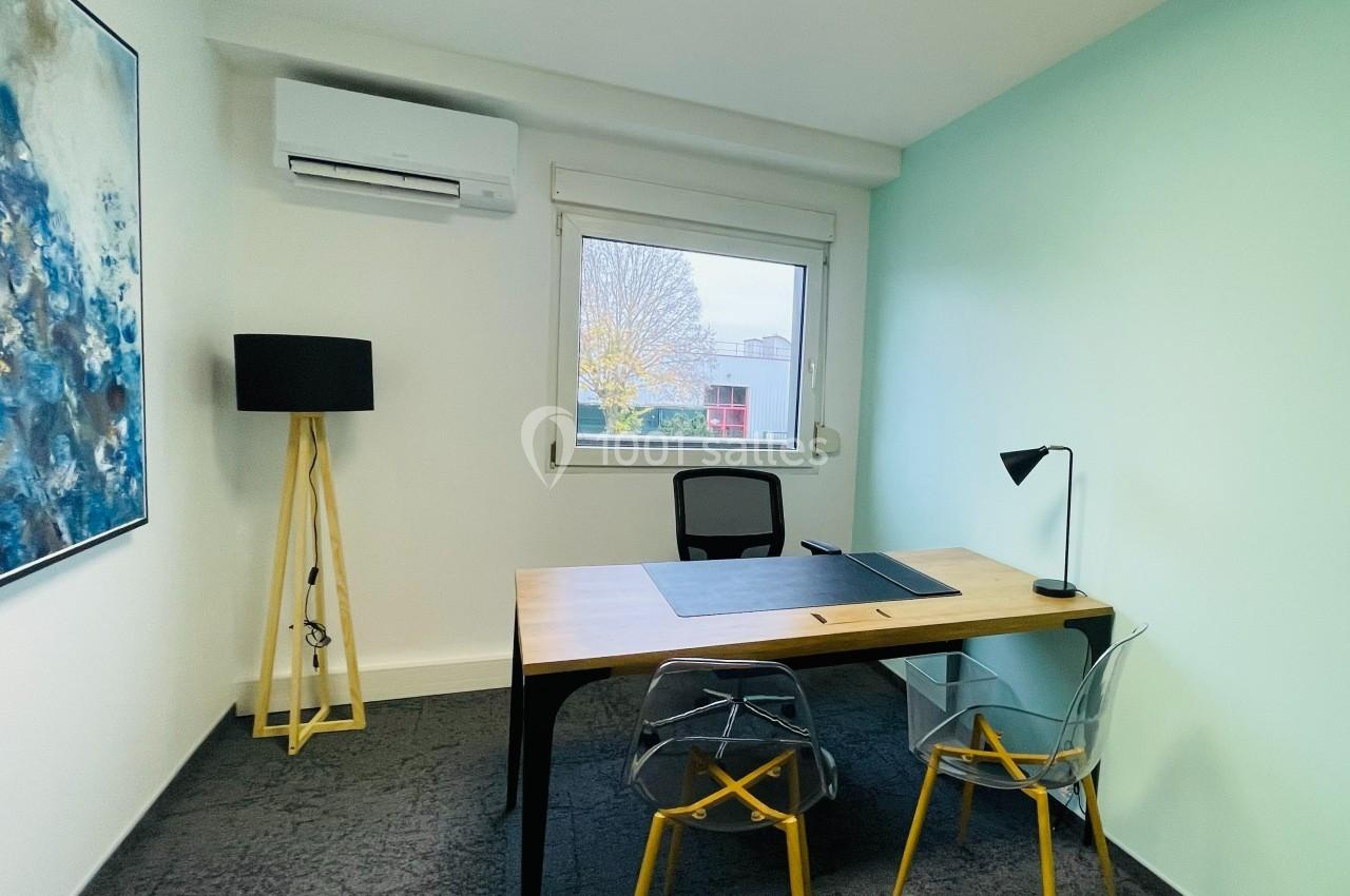 Bureau lumineux avec un bureau en bois, deux chaises, une lampe de bureau, un tableau et une fenêtre donnant sur l'extérieur.