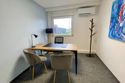 Salle de réception avec tables rondes dressées, nappes blanches, serviettes rouges et chaises grises sur parquet clair.