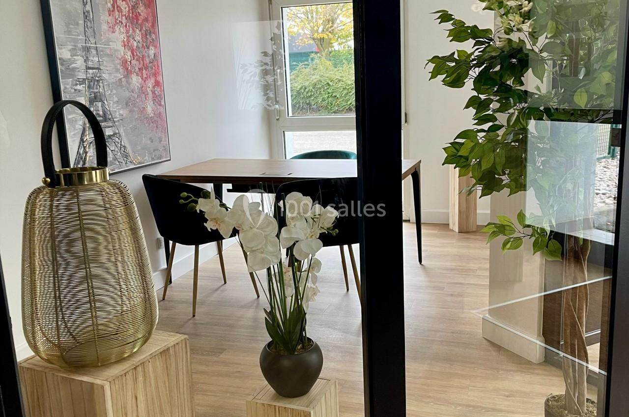 Salle lumineuse avec table en bois, chaises noires, plantes décoratives et tableau mural représentant la Tour Eiffel.