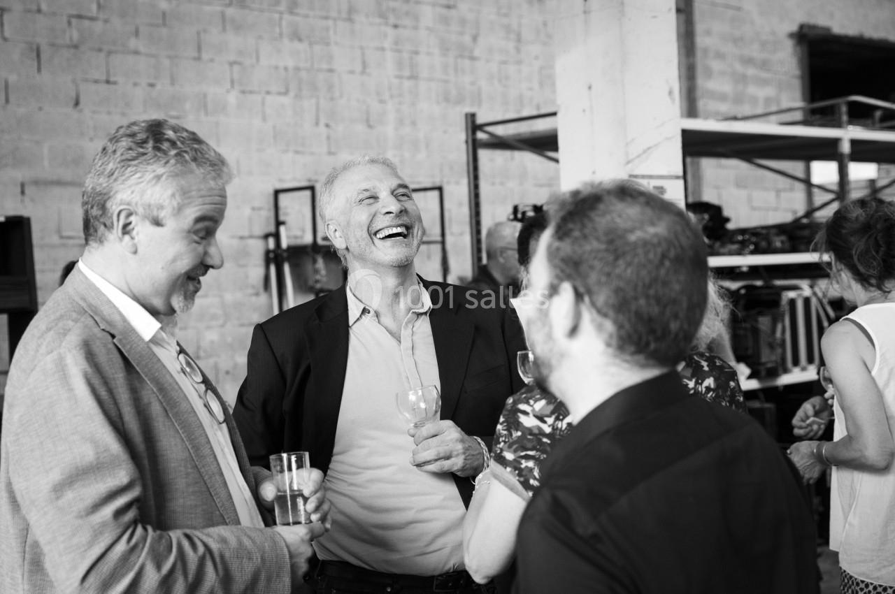 Des personnes discutent et rient lors d'un événement convivial dans un espace intérieur avec des étagères en arrière-plan.