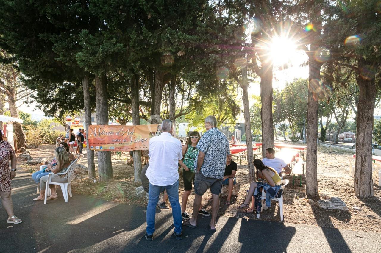 Groupe de personnes discutant et se relaxant sous des arbres, avec une lumière de soleil filtrant à travers les branches.