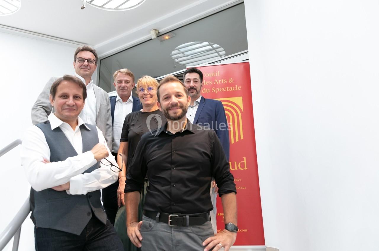 Un groupe de six personnes posant devant une bannière rouge dans un espace intérieur lumineux.