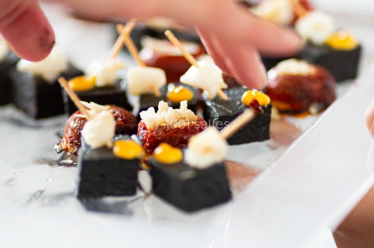 Des mains disposant des amuse-bouches sur un plateau, composés de morceaux noirs, garnis de fromage et de tomates.