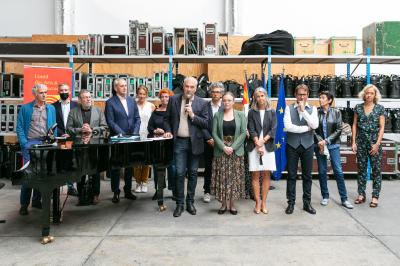 Une main verse du vin blanc dans un verre transparent, avec des bouteilles en arrière-plan flou.