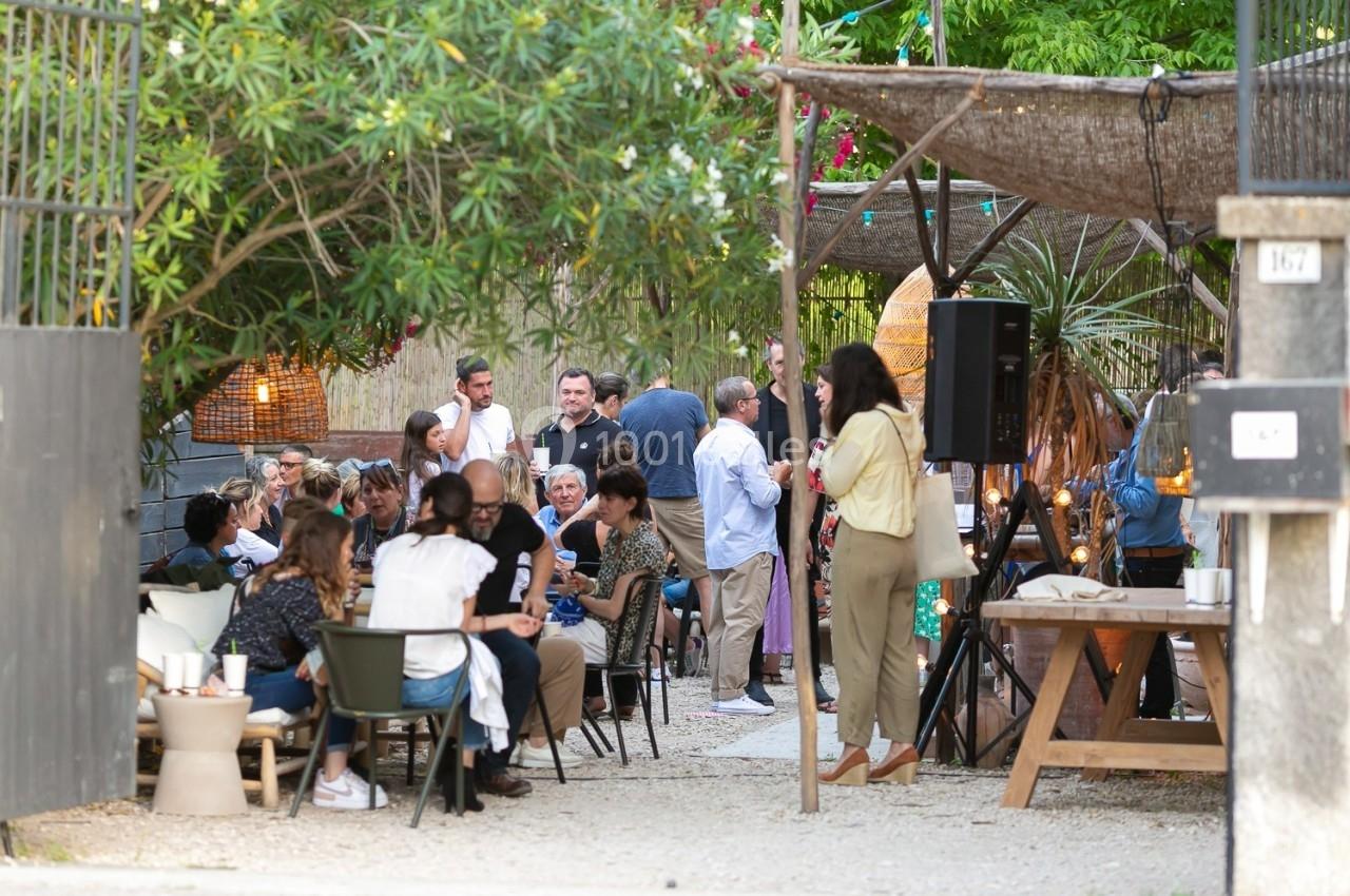 Groupe de personnes assises et debout dans une cour extérieure, discutant et partageant un moment convivial.