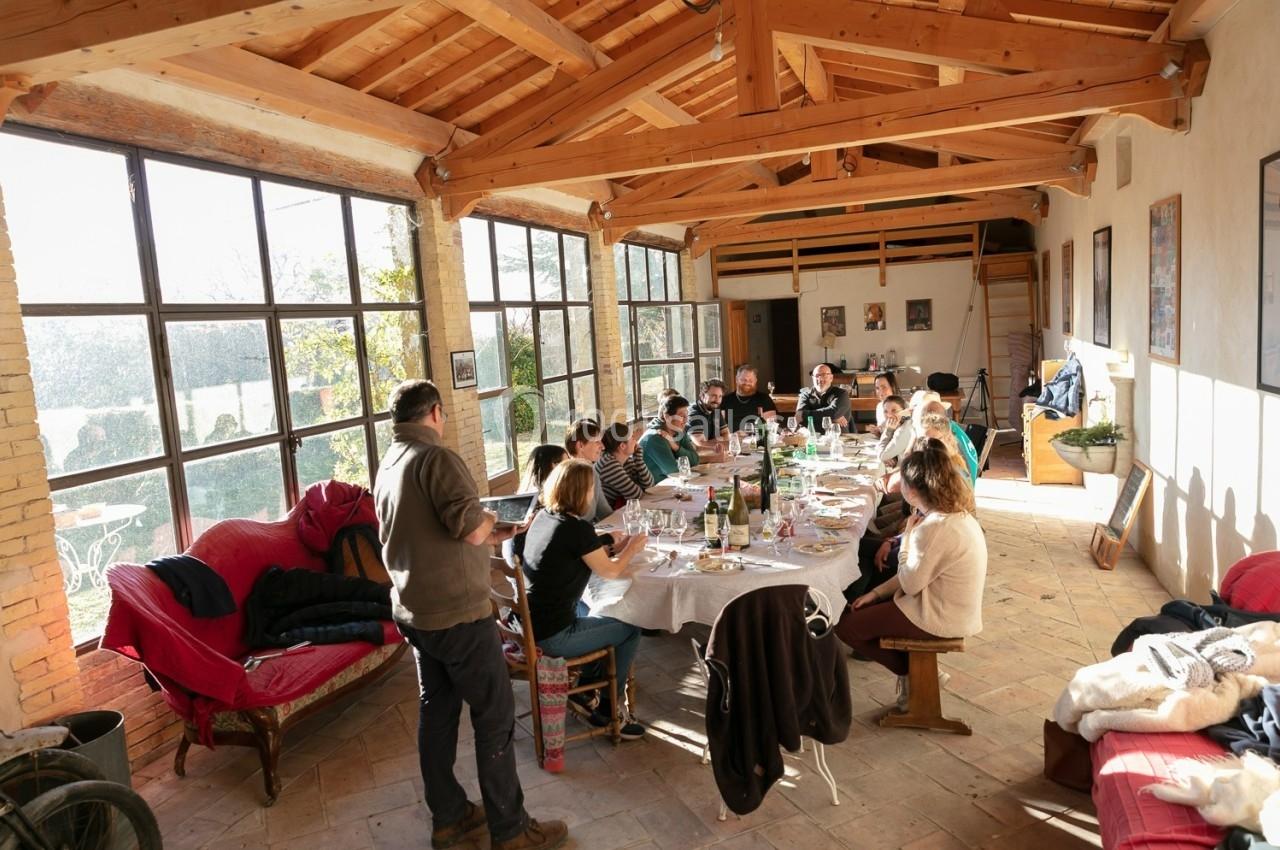 Un groupe de personnes partage un repas autour d'une grande table dans une salle lumineuse avec des poutres en bois.