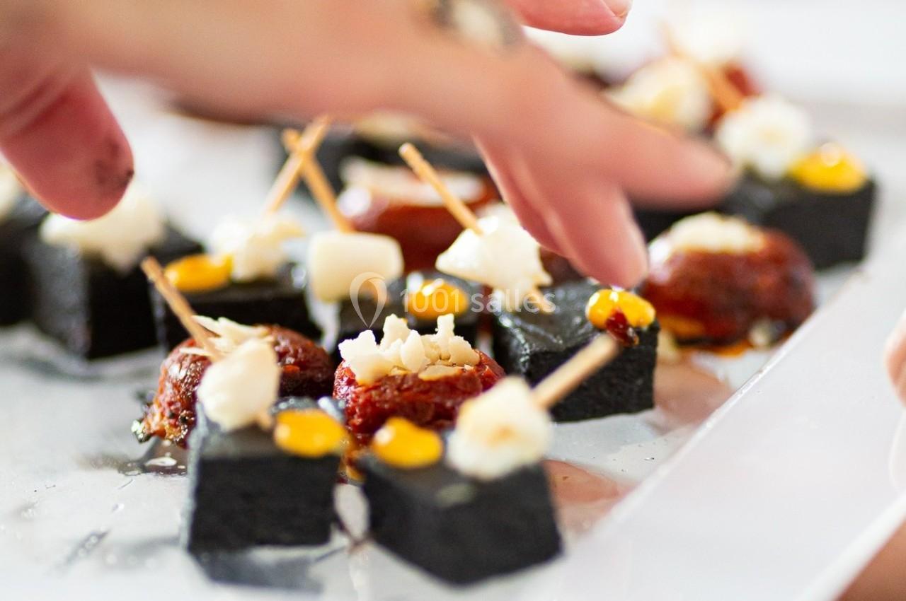 Des amuse-bouches élégants composés de cubes noirs, tomates séchées et garnitures, présentés sur un plateau.
