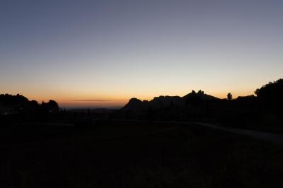 Paysage au crépuscule avec silhouettes de collines, arbres et habitations sous un ciel dégradé du bleu à l'orange.