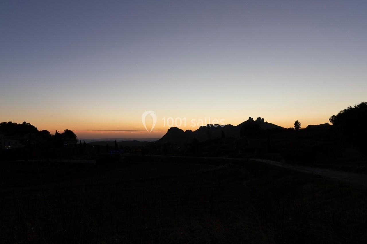 Paysage au crépuscule avec silhouettes de collines, arbres et habitations sous un ciel dégradé du bleu à l'orange.