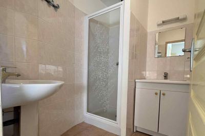 Salle de bain avec lavabo, miroir, meuble blanc et douche à paroi vitrée sur un carrelage beige.