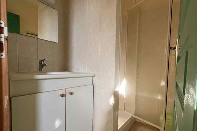 Salle de bain avec lavabo, miroir, meuble blanc et douche à paroi vitrée sur un carrelage beige.
