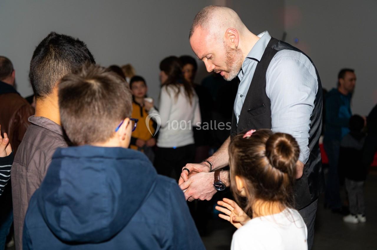Un homme réalise un tour de magie devant un groupe d'enfants dans une salle animée.