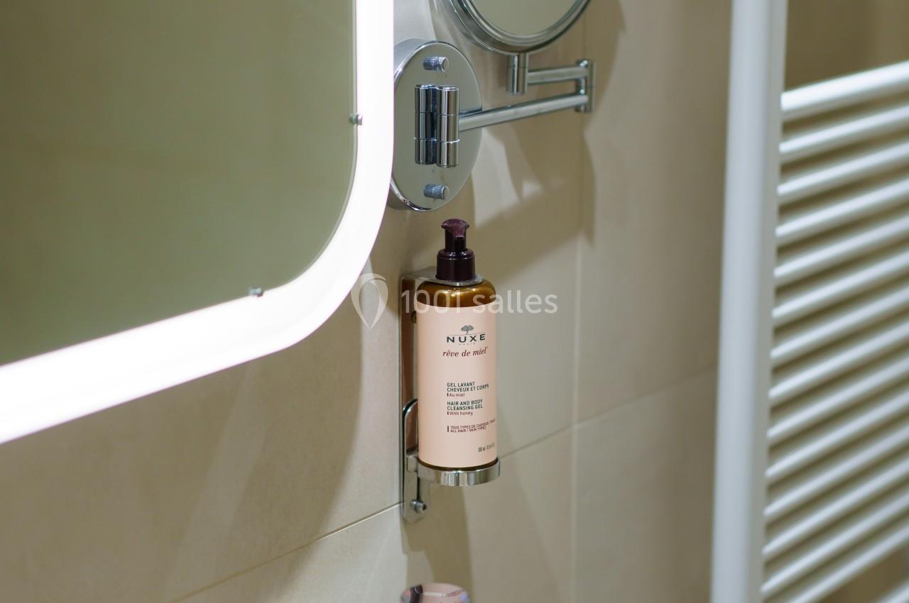 Miroir lumineux, miroir grossissant, distributeur de savon et robinet sur un lavabo dans une salle de bain moderne.