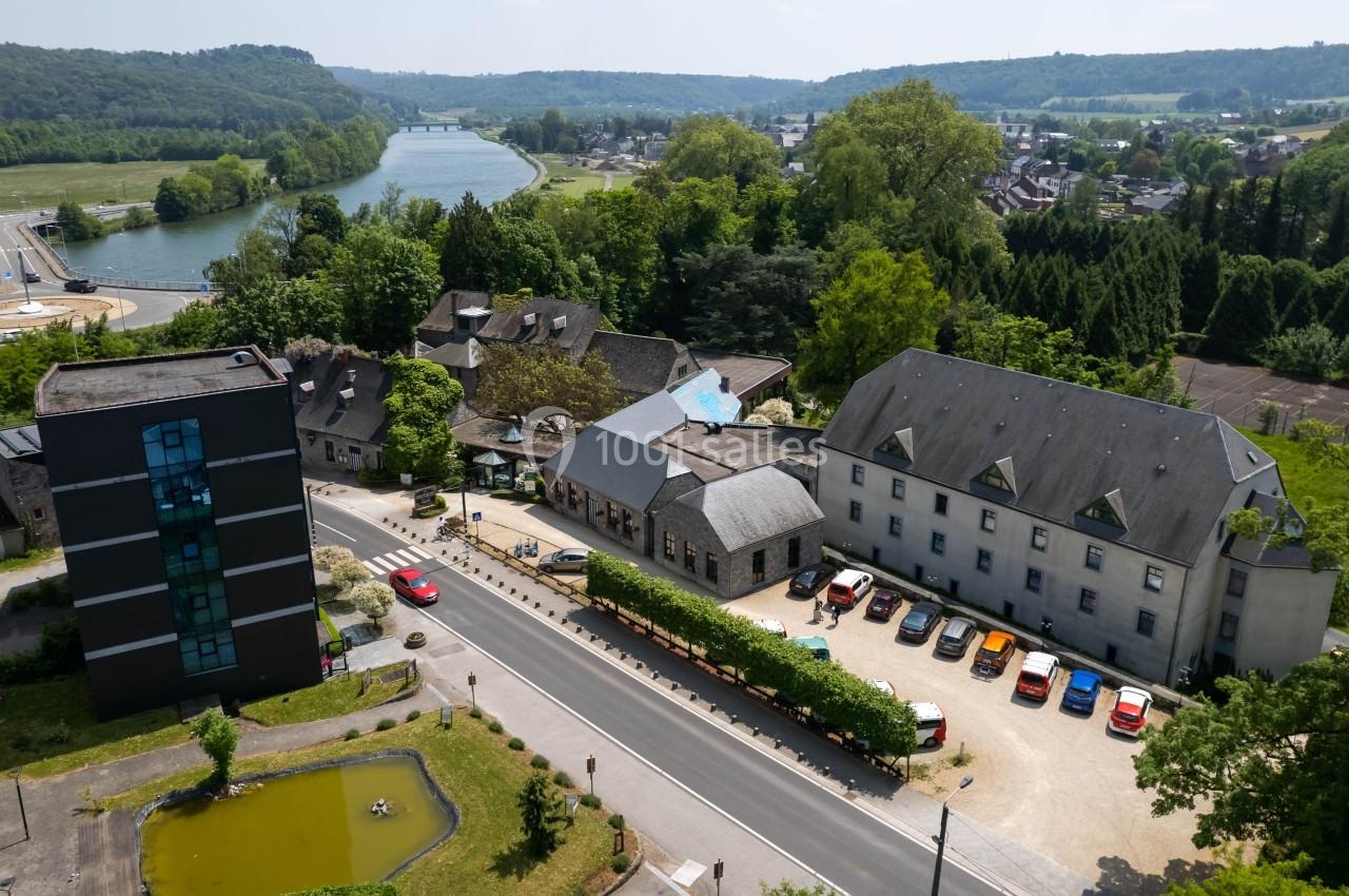 Vue aérienne d'un complexe de bâtiments entouré de verdure, avec une route et une rivière à proximité.