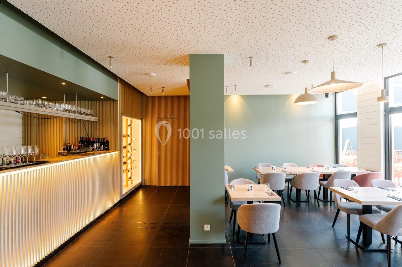 Salle de restaurant moderne avec un bar éclairé, des tables dressées et des chaises rembourrées dans un décor épuré.