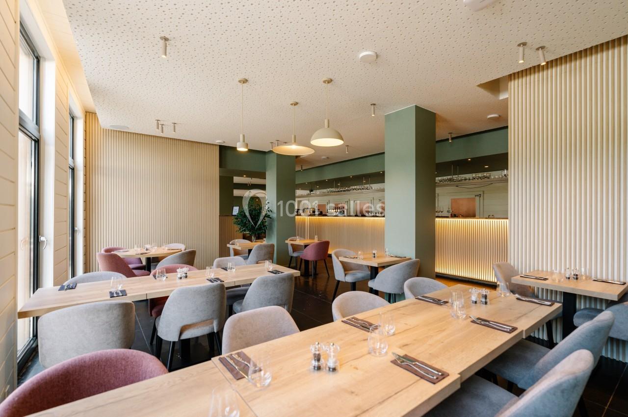 Salle de restaurant moderne avec tables en bois, chaises colorées et éclairage suspendu, vue sur un comptoir en arrière-plan.